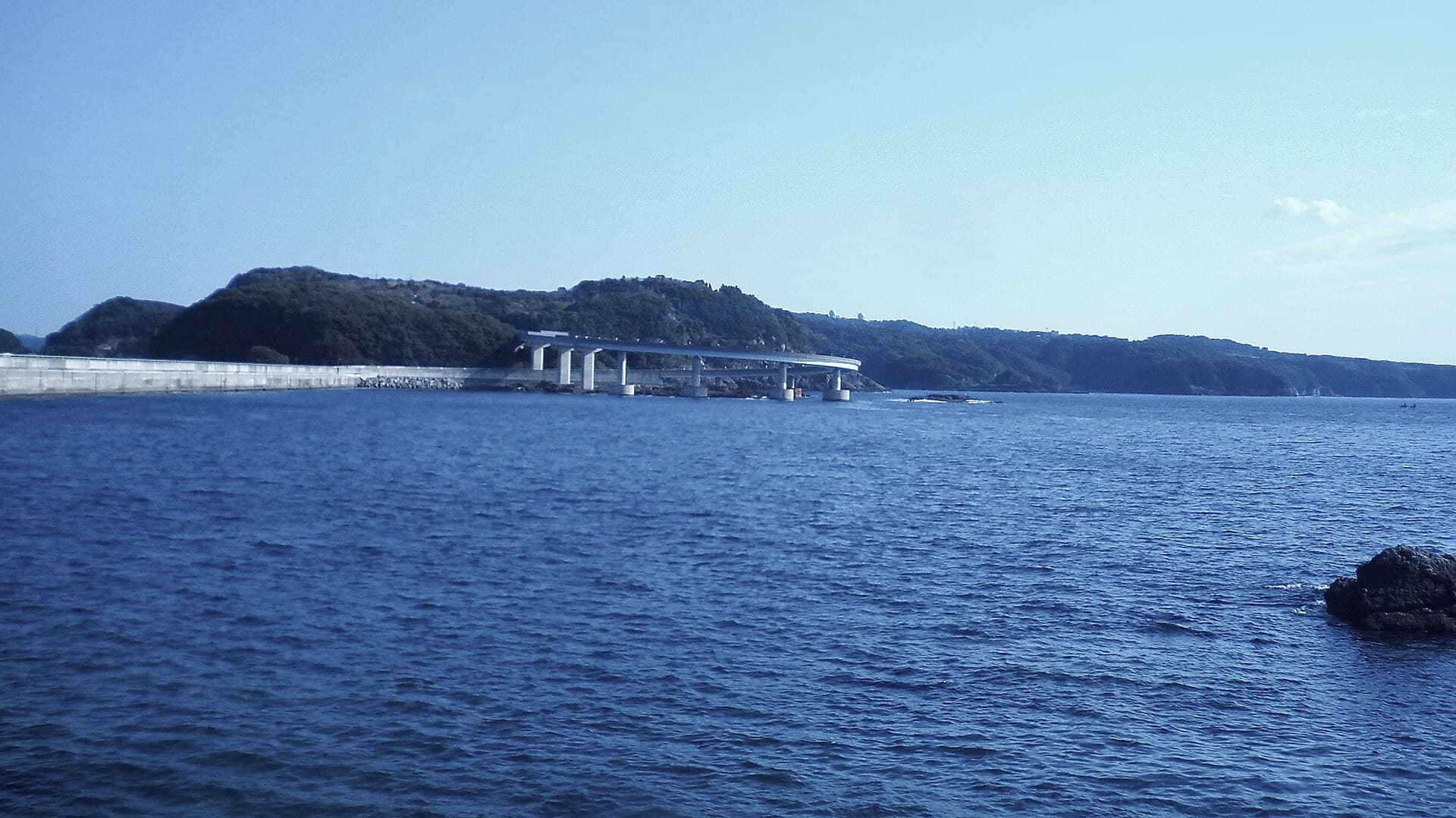 串本大桥：串本大桥：Wikimedia Commons 文件「Kushimoto Bridge View from Shiono Misaki 20100214a.JPG」中的桥梁实景。